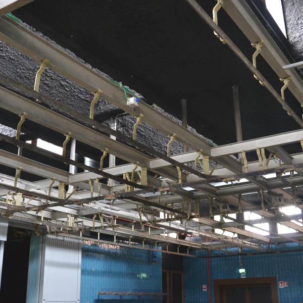Foto soffitto con binari di metallo e parete con piastrelle azzurre delle Ex Celle Frigo di Officina Giovani.