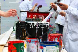 Particolare del laboratorio di writing art all\'Istituto Livi Brunelleschi: le mani dei ragazzi che usano pennelli e intingono nei secchi di vernice colorata.