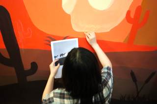 Particolare di un murales a tema naturale con un canyon al tramonto dell\'Istituto Livi Brunelleschi - via Galcianese mentre viene realizzato da uno studente con in mano il bozzetto di un cammello.