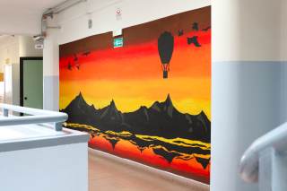 Murales del Gramsci-Keynes con ritratto paesaggio montano al tramonto e una mongolfiera che sta volando nel cielo circondata dagli uccelli.