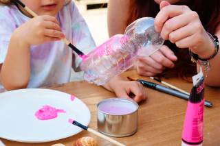 bambina che dipinge di rosa una bottiglietta di plastica