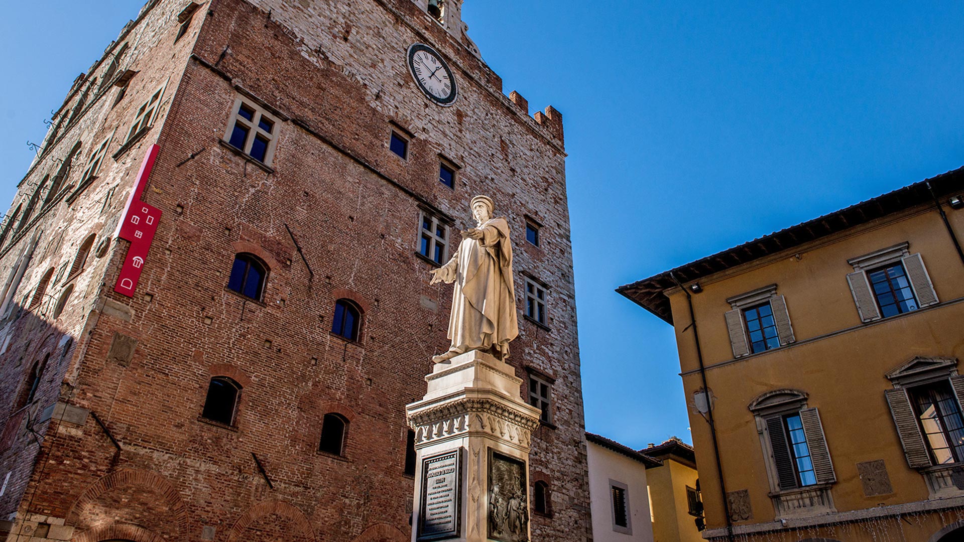 Ripresa dal basso verso l\'alto della statua di Datini in mezzo a piazza del Comune, sullo sfondo il Museo di Palazzo Pretorio