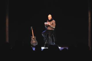 l\'attore è seduto con in mano un foglietto di carta