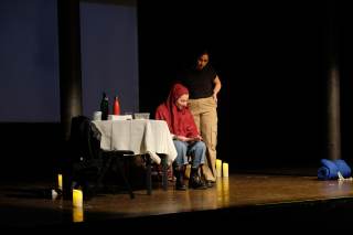 Foto dello spettacolo. Una delle due attrici &egrave; seduta, l\'altra la guarda in piedi al suo fianco.