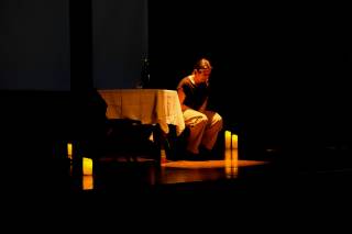 Foto dello spettacolo. Un\'attrice piange seduta su una sedia.