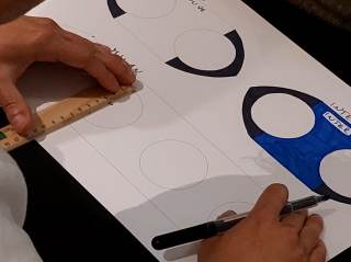 Foto di un ragazzo che misura e colora su un foglio di carta durante il laboratorio.