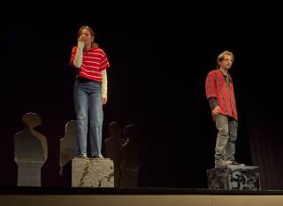 Foto dello spettacolo. I due attori sono ai lati opposti del palco.